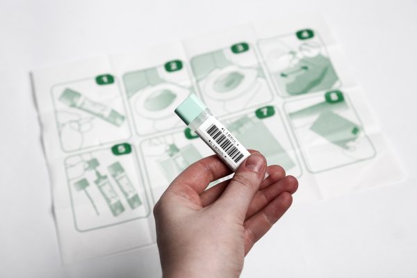 Eine Person hält einen Darmkrebs-Selbsttest in der Hand. Im Hintergrund liegt ein Infoflyer zur korrekten Durchführung des Test