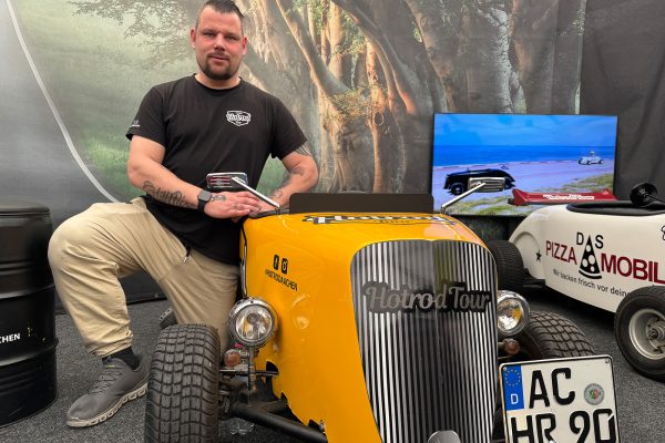 Sascha Vogel kniet neben einer gelben Hotrod-Mini-Seifenkiste mit Straßenzulassung
