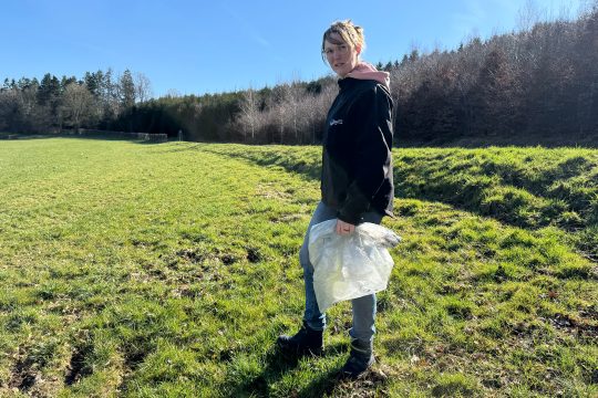 Landwirtin Belinda Geiben steht auf einem Feld und hält einen Müllsack in den Händen