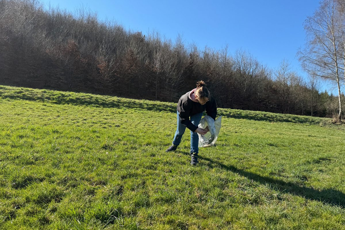 Landwirtin Belinda Geiben steht auf einem Feld und sammelt Müll in eine Tüte