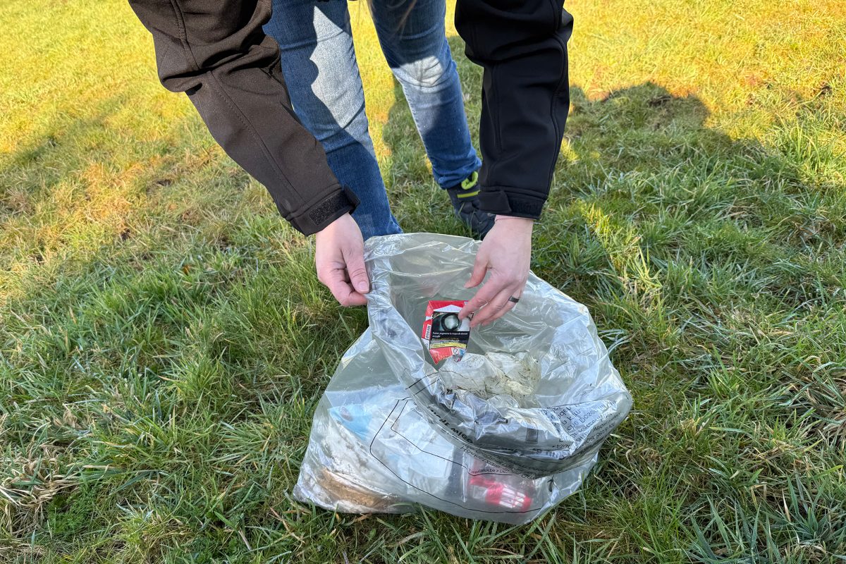 Landwirtin Belinda Geiben steht auf einem Feld und sammelt Müll in eine Tüte