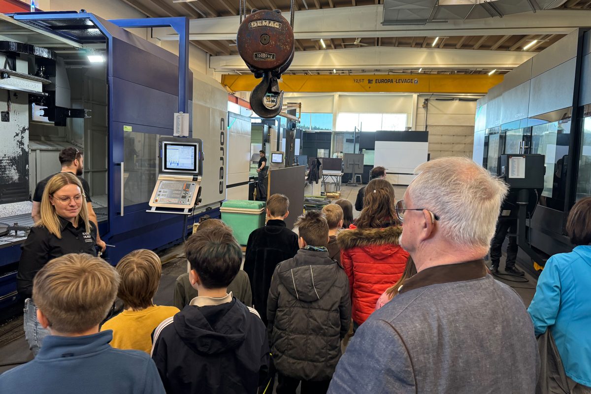 Die Kinder lassen sich in der Produktionshalle mit diversenen Maschinen von Mitarbeitern etwas erklären