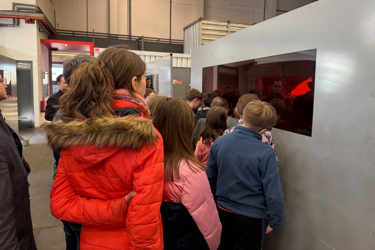 Die Kinder lassen sich in der Produktionshalle mit diversenen Maschinen von Mitarbeitern etwas erklären