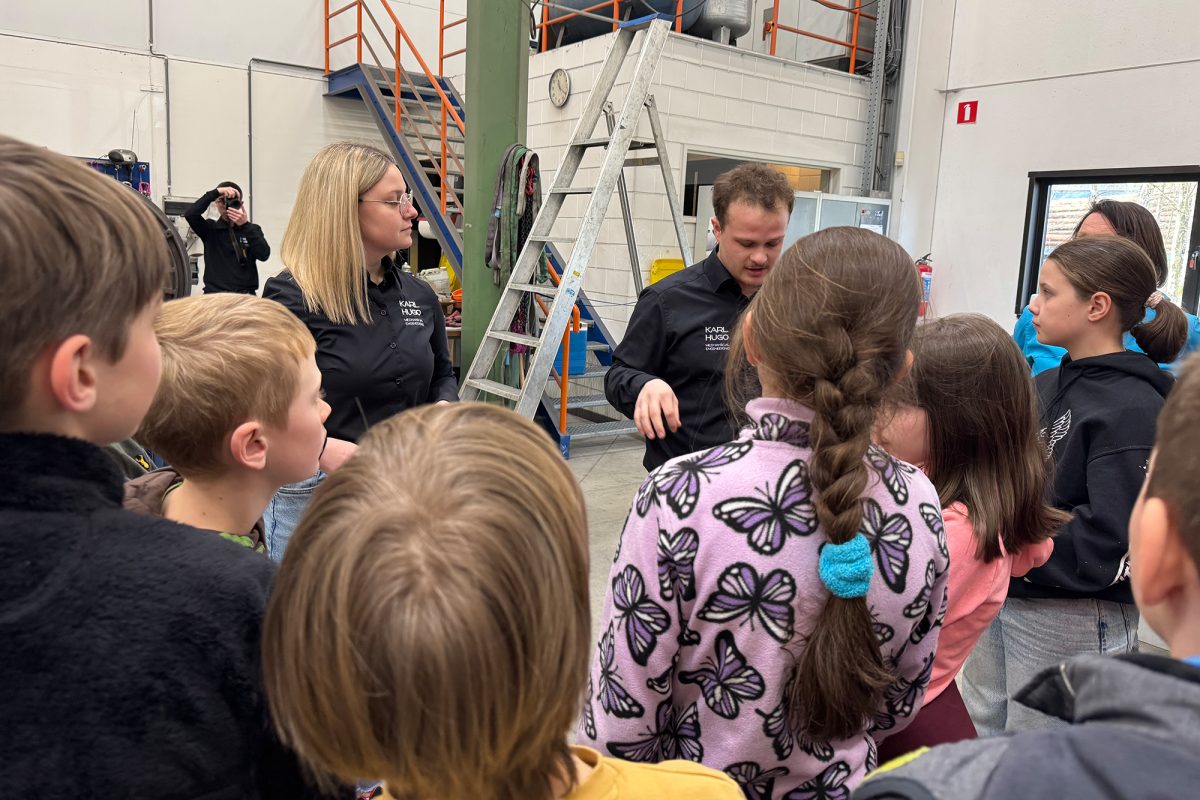 Die Kinder lassen sich in der Produktionshalle mit diversenen Maschinen von Mitarbeitern etwas erklären