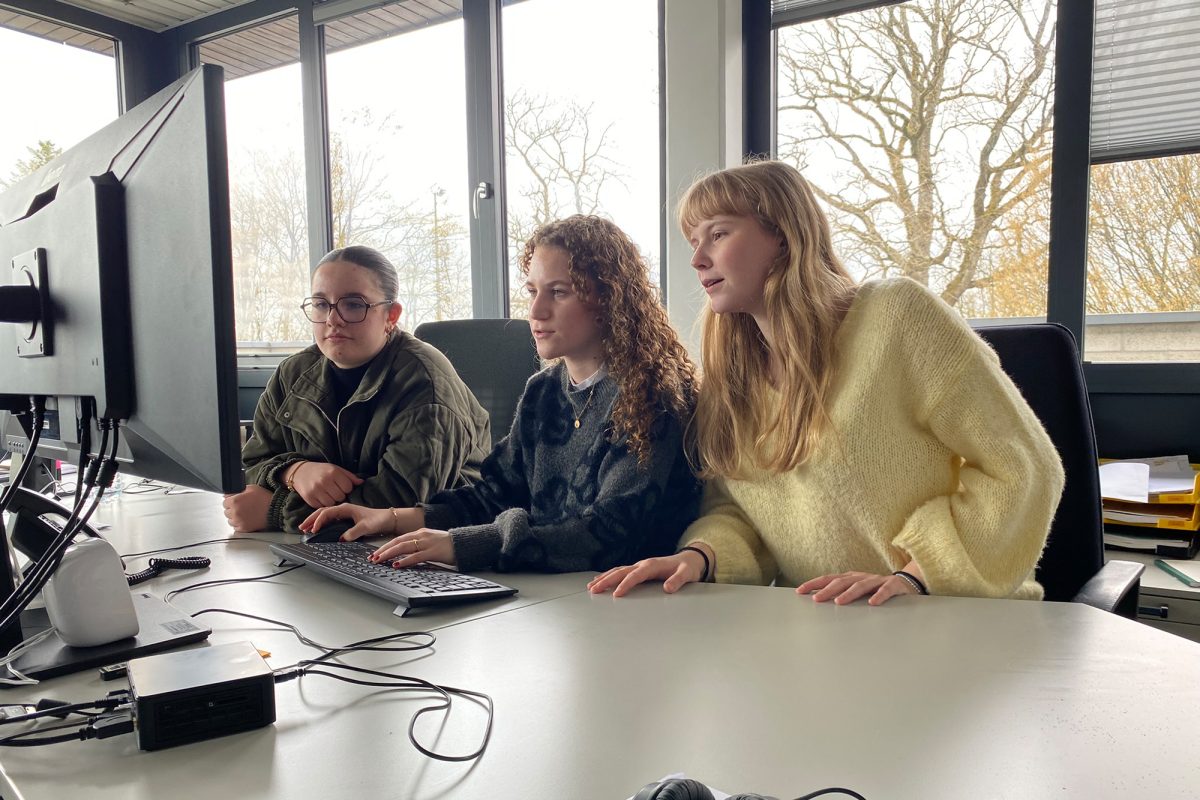 Siennaa, Claire und Liesl von der MG St. Vith sitzen im Redaktionsbüro des BRF an einem Schreibtisch und schauen auf den Monitor