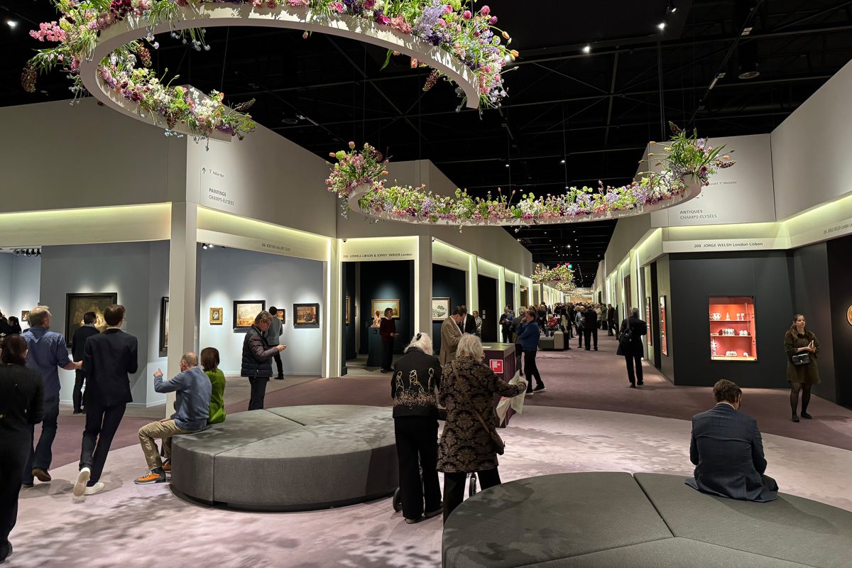 Einige Messebesucher sitzen auf Polstermöbeln, von der Decke hängen mit Blumen bepflanzte Halbkreise