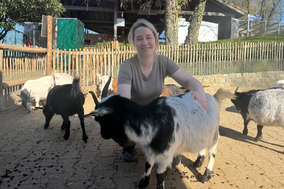 Janina Dötzer ist im Streichelgehege, sie kniet neben einer Ziege und lächelt