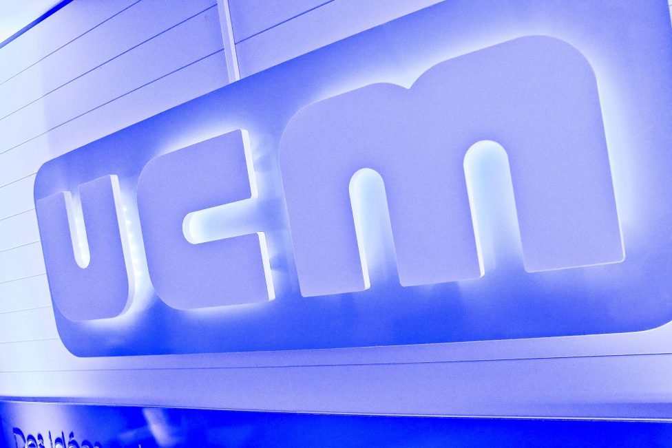 Die drei Buchstaben UCM in weiß, im Hintergrund strahlt blaues Licht