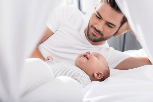 Vater mit lachendem Baby liegen auf einem Bett
