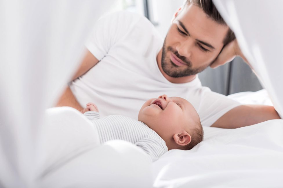 Vater mit lachendem Baby liegen auf einem Bett