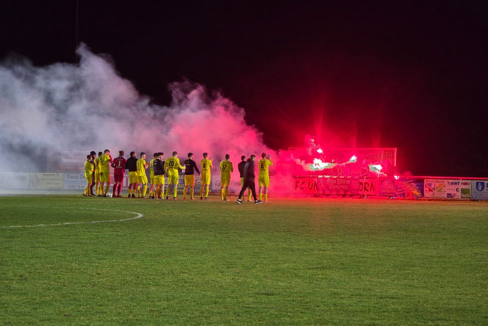 Spieler des KFC Weywertz jubeln den Fans zu, die bengalisches Feuer zünden