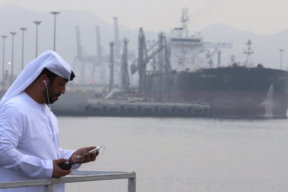 Ein arabischer Mann mit Smartphone und Ohrhörern steht im Öl-Hafen