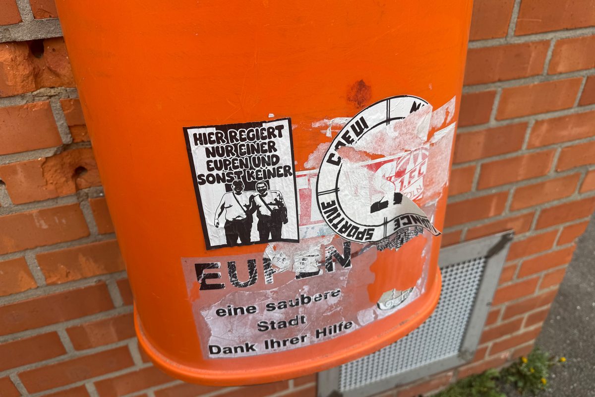 Ein oranger Mülleimer der Stadt, auf dem mehrere Aufkleber haften.