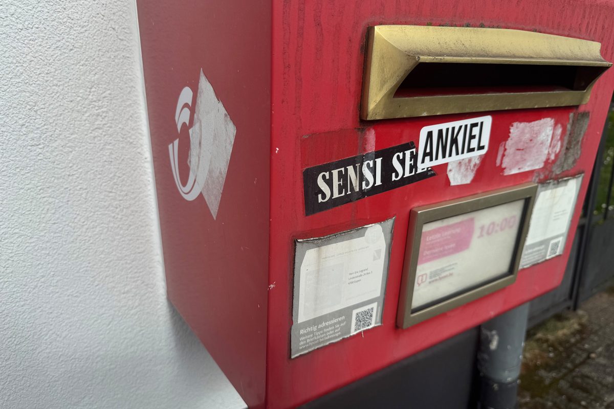 Ein Briefkasten der Post, auf dem mehrere Aufkleber, zum Teil übereinander, haften