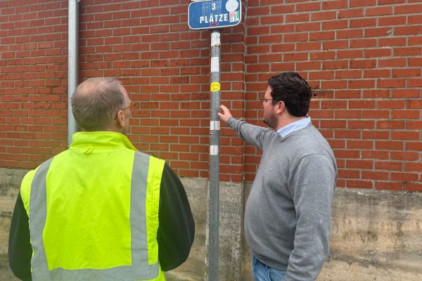 Christian Collard und Lucas Reul stehen vor dem Mast eines Straßenschildes, der mit verschiedenen Aufklebern beklebt ist