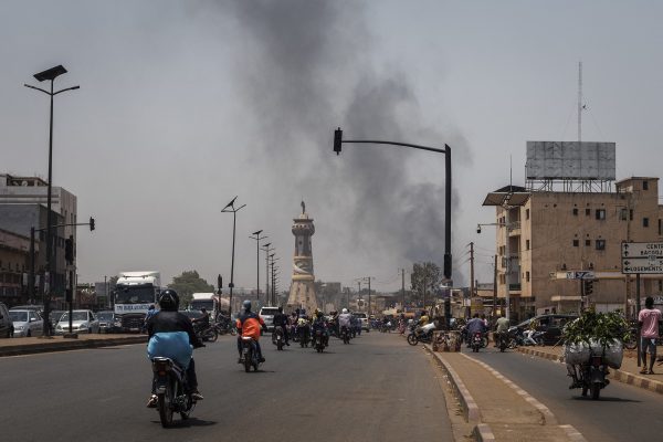 Menschen auf Mopeds auf einer der Hauptstraßen von Bamako, im Hintergrund sind Rauchschwaden zu sehen