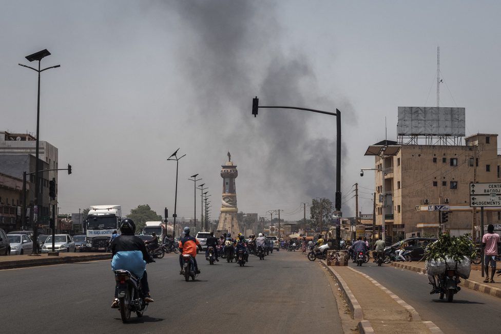 Menschen auf Mopeds auf einer der Hauptstraßen von Bamako, im Hintergrund sind Rauchschwaden zu sehen