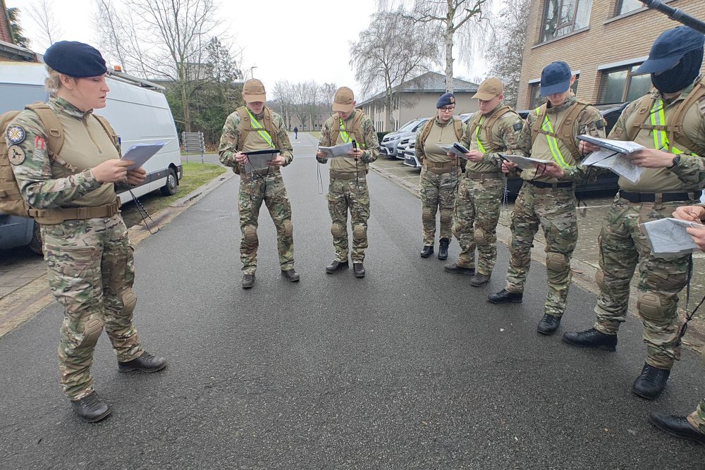 eine Frau in Militäruniform spricht zu mehreren jungen Menschen in Uniform. Sie schauen auf die Karten in ihren Händen