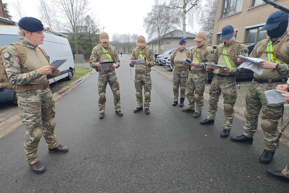 eine Frau in Militäruniform spricht zu mehreren jungen Menschen in Uniform. Sie schauen auf die Karten in ihren Händen