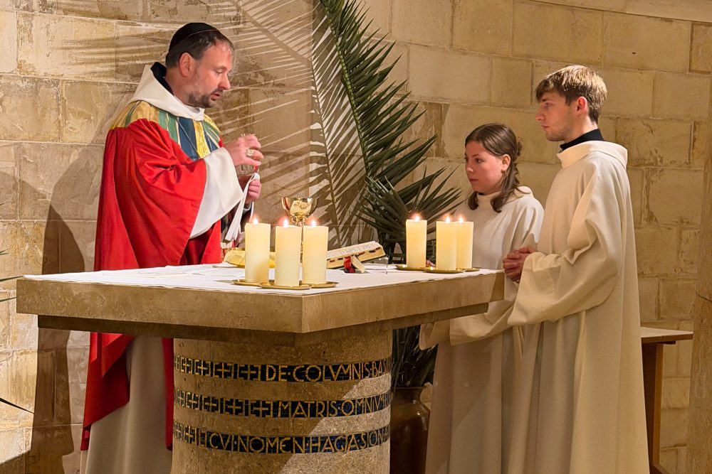 Abt Nikodemus Schnabel bei der Feier am Palmsonntag in der Abtei Dormitio in Jerusalem, er steht hinter dem Altar und hat die Hände zum Gebet gefaltet, zwei Messdiener stehen neben ihm