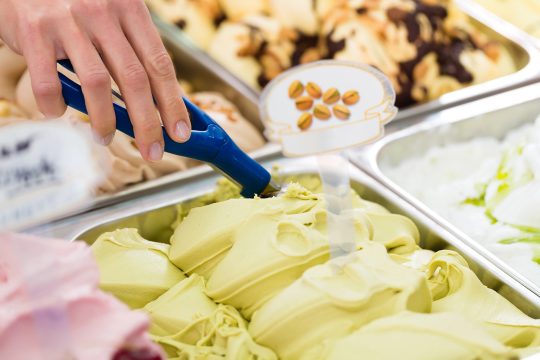 Verschiedene Eissorten in der Theke eines Eiscafés, eine Hand bei der Arbeit