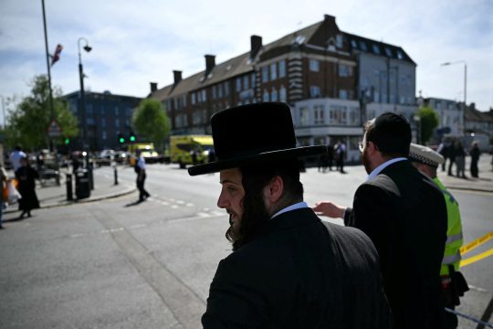Zwei jüdische Anwohner beobachten von außerhalb eines abgesperrten Bereichs im Stadtteil Golders Green im Norden Londons das Geschehen. Einer der beiden Männer spricht mit einem Polizeibeamten