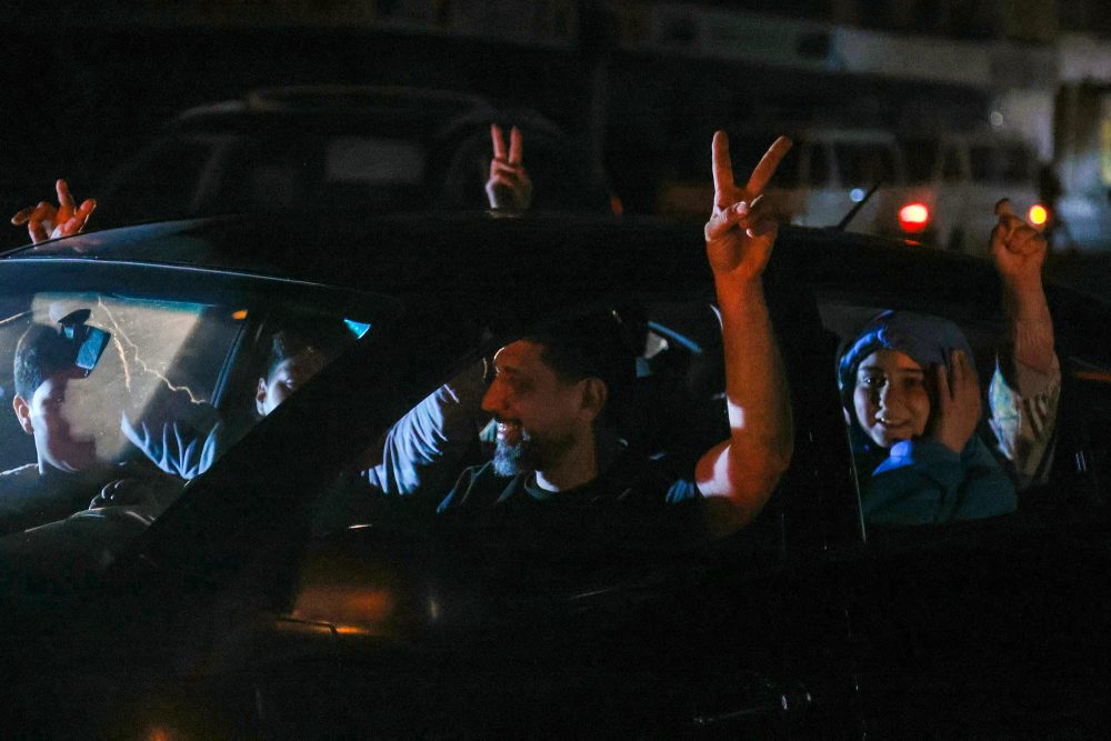 Menschen sitzen in einem Auto und jubeln, indem sie die Arme herausstrecken und mit zwei Fingern das Victory-Zeichen bilden