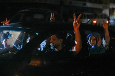 Menschen sitzen in einem Auto und jubeln, indem sie die Arme herausstrecken und mit zwei Fingern das Victory-Zeichen bilden