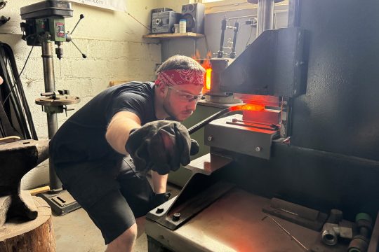 Messermacher Joé Onderbeke mit rotem Kopftuch und dicken Handschuhen ausgerüstet arbeitet am Metallofen