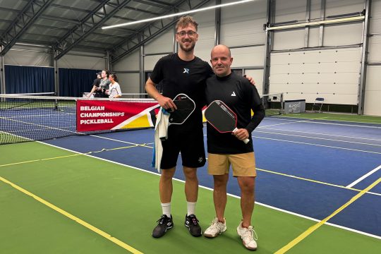 Björn Bemelmans (re.) und Boris Paque stehen mit Schlägern auf dem Spielfeld und lächeln in die Kamera