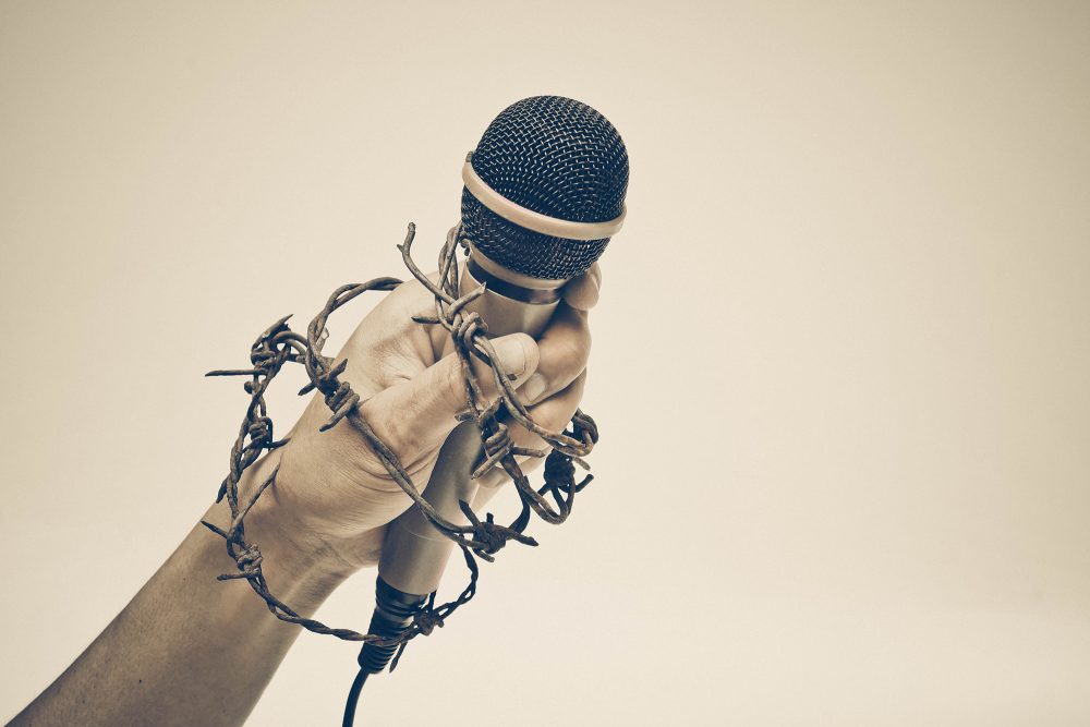 Hand mit Mikro und Stacheldraht