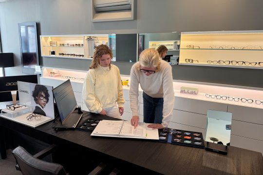 Caroline Pankert beugt sich über einen Katalog und zeigt Thea Cormann darin etwas