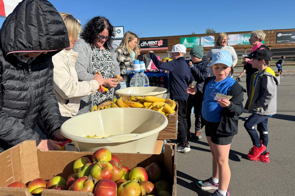 An einem Stand verteilen einige Frauen Äpfel und Bananen an die Kinder aus