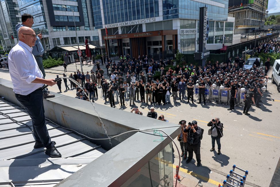 Mahmut Tanal steht auf dem Dach der Parteizentrale, einen Wasserschlauch in der Hand. Vor der Zentrale steht eine Menschenmenge, an der Seite etliche Polizisten mit Schilden