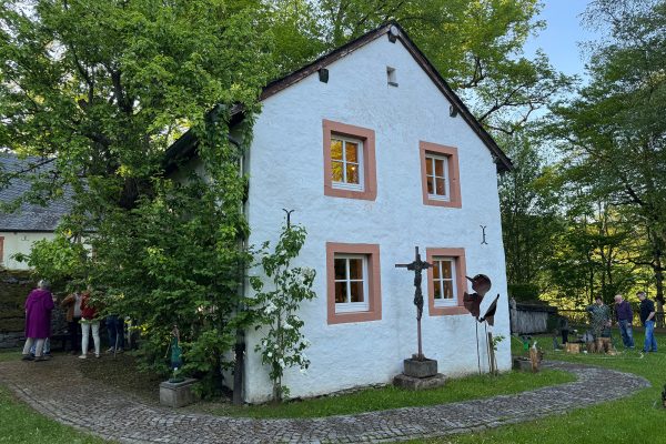 Außenansicht der Einsiedelei Wiesenbach, neben dem Gebäude stehen ein paar Menschen