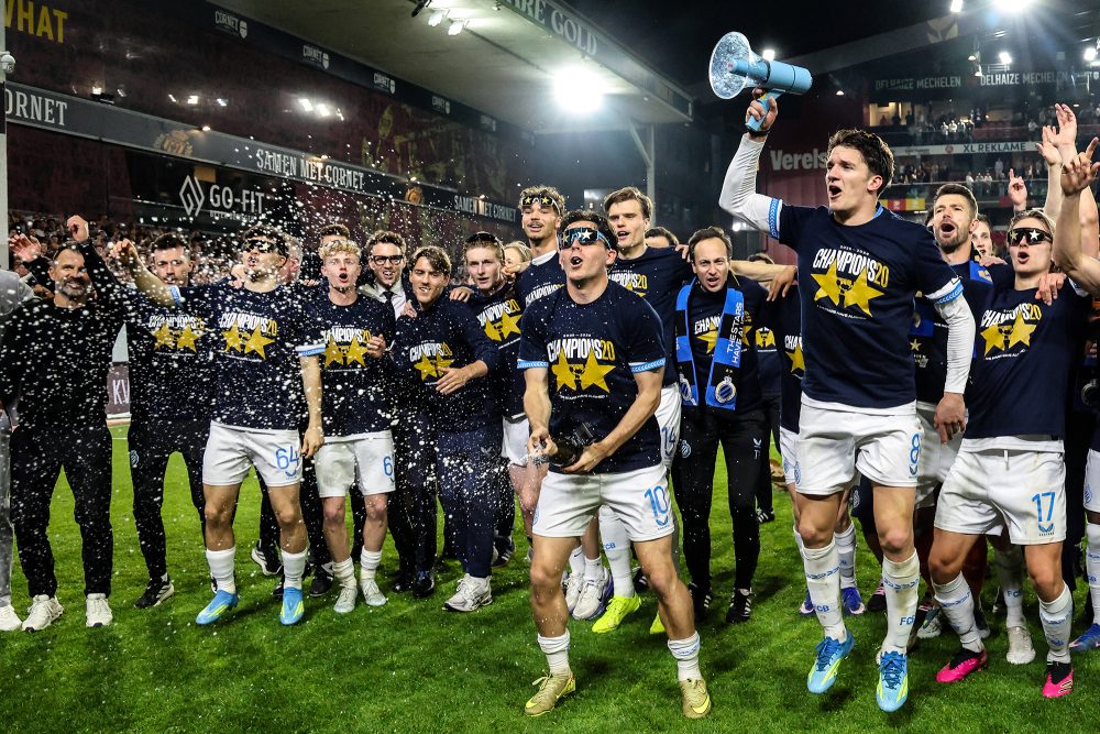Spieler des FC Brügge stehen auf dem Stadionrasen und jubeln, einer hält ein Megafon in der Hand, Konfetti schwebt in der Luft