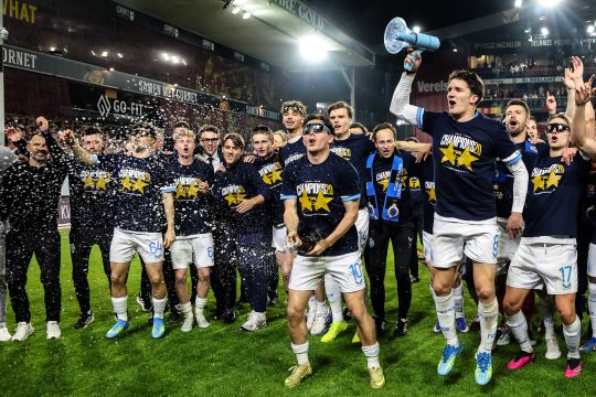Spieler des FC Brügge stehen auf dem Stadionrasen und jubeln, einer hält ein Megafon in der Hand, Konfetti schwebt in der Luft