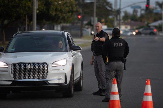 Polizisten sprechen mit einem Autofahrer, neben ihnen stehen Absperrhütchen auf dem Boden