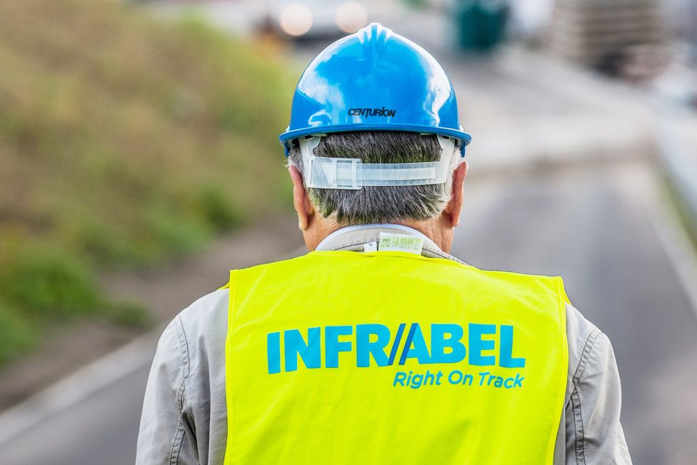 Hinteransicht eines Arbeiters mit blauem Helm und gelber Leuchtweste mit dem Aufdruck "Infrabel"