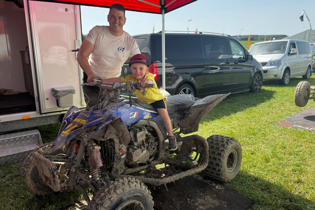 Quadfahrer Mathias Heyen steht neben einem Quad, auf dem ein kleines Kind sitzt - beide lächeln in die Kamera