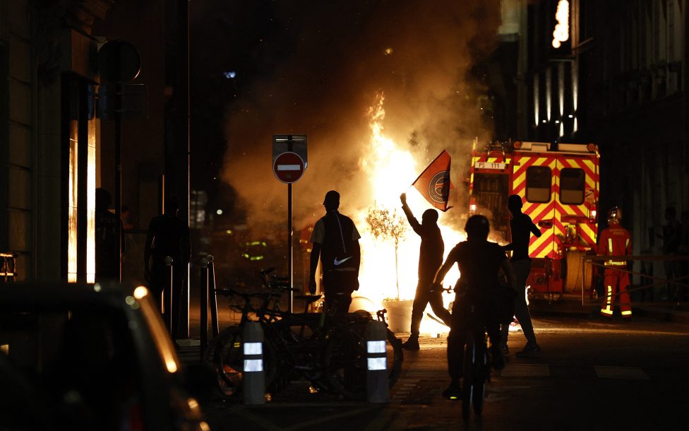 Brennende Barrikade im 16. Arrondissement von Paris, einige Personen stehen davor, ein Mann hält eine Flagge von Paris-Saint-Germain hoch