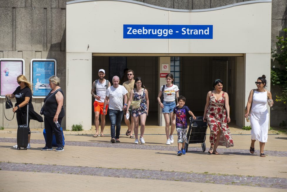 Menschen kommen aus dem Bahnhof "Zeebrugge-Strand", sie tragen sommerliche Kleidung
