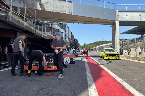 Der Ford Escort RS 1600 1972 vor der Box von LifeLive, rechts fährt ein BMW die Boxengasse hinunter