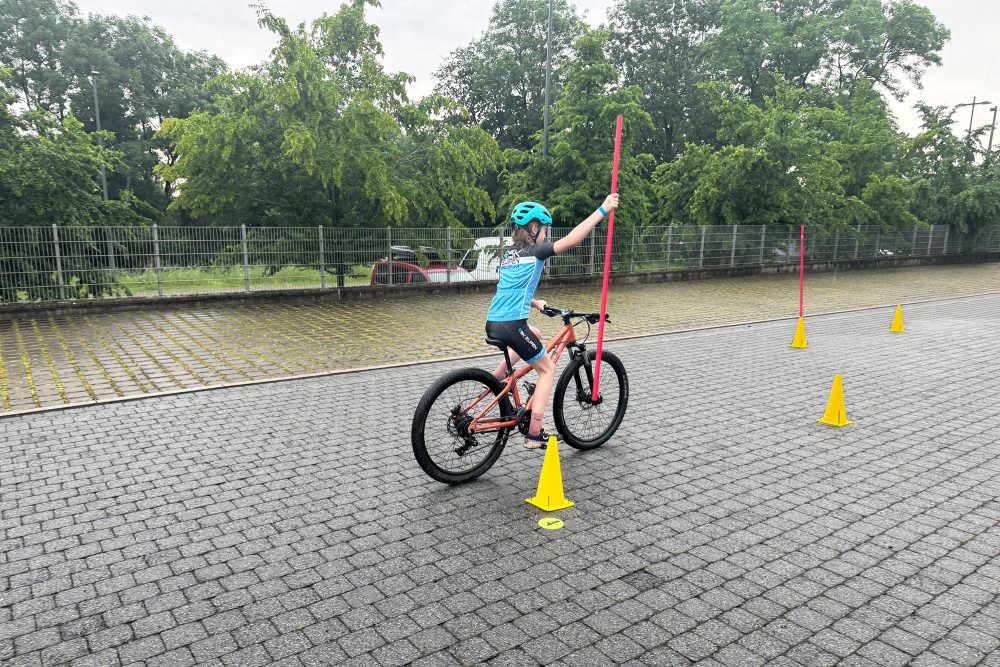Kind fährt einhändig auf einem Fahrrad und hält eine Stange in der anderen Hand