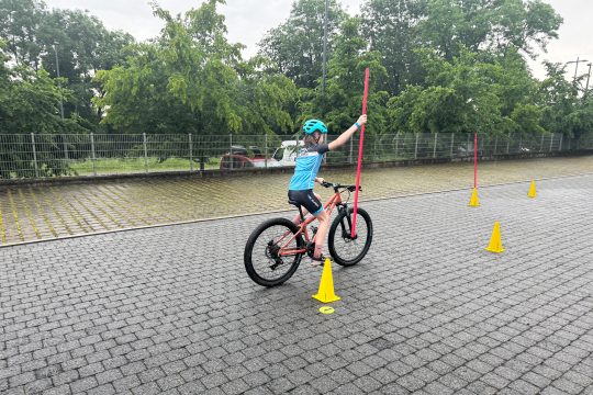 Kind fährt einhändig auf einem Fahrrad und hält eine Stange in der anderen Hand