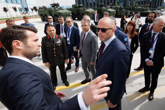 Verteidigungsminister Theo Francken und weitere Mitglieder der belgischen Delegation stehen im Halbkreis um den Verantwortlichen einer türkischen Rüstungsfirma