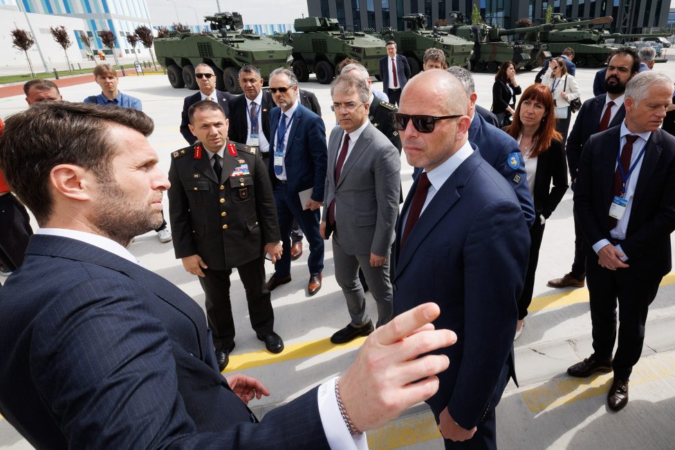 Verteidigungsminister Theo Francken und weitere Mitglieder der belgischen Delegation stehen im Halbkreis um den Verantwortlichen einer türkischen Rüstungsfirma