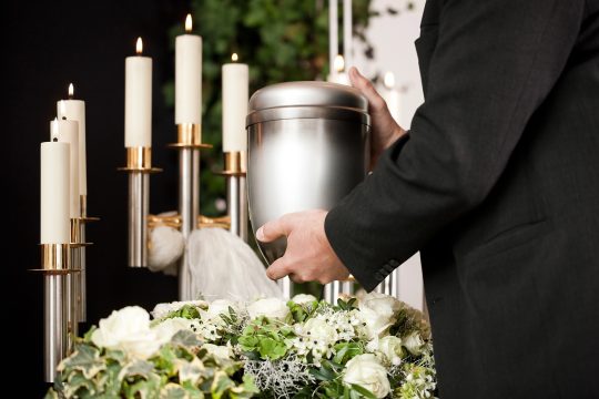 Bestatter mit Urne, im Hintergrund sieht man Kerzen und Blumen
