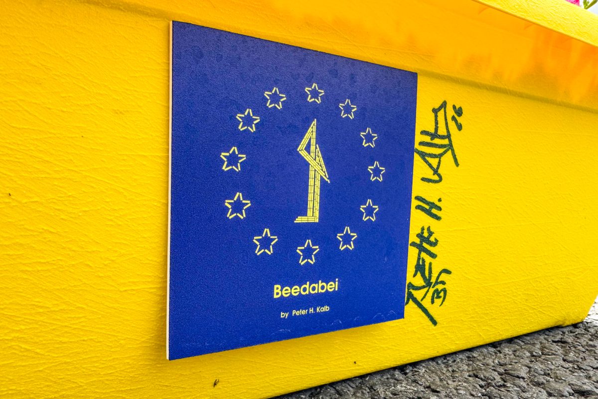 Logo von "Beedabei" gelb auf blauem Hintergrund, angebracht auf einem gelben Blumenkasten