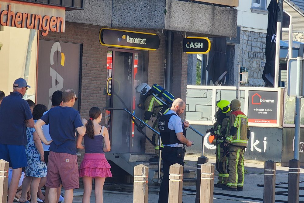 Ein Feuerwehrmann betritt die Räumlichkeit, davor stehen weitere Feuerwehrleute, mit etwas Abstand stehen Passanten
